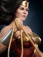 Portrait of a female superhero wearing a gold tiara with a red star and red armor, gripping the golden lasso coiled in her hand against a dark background.