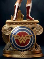 Golden pedestal featuring a large Wonder Woman shield with boots standing atop ornate spiraled wings and stone base.