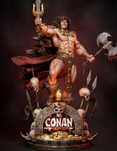 Tall muscular Conan the Barbarian statue stands on a skull-adorned pedestal, cape flowing, with a spear raised in one hand and a battle-axe in the other.