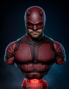 Bust of Daredevil in a red suit and horned helmet against a dark background, from chest up on a red pedestal.