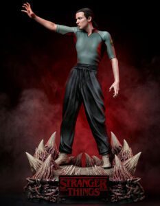 Action figure of Eleven from Stranger Things, standing with one arm extended on a spiked, rocky base with red fog.