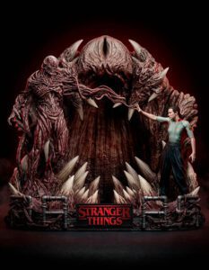 Diorama of a massive red, spiked creature with an open mouth, a man in a green shirt reaching toward it, and a 'Stranger Things' sign at the base.
